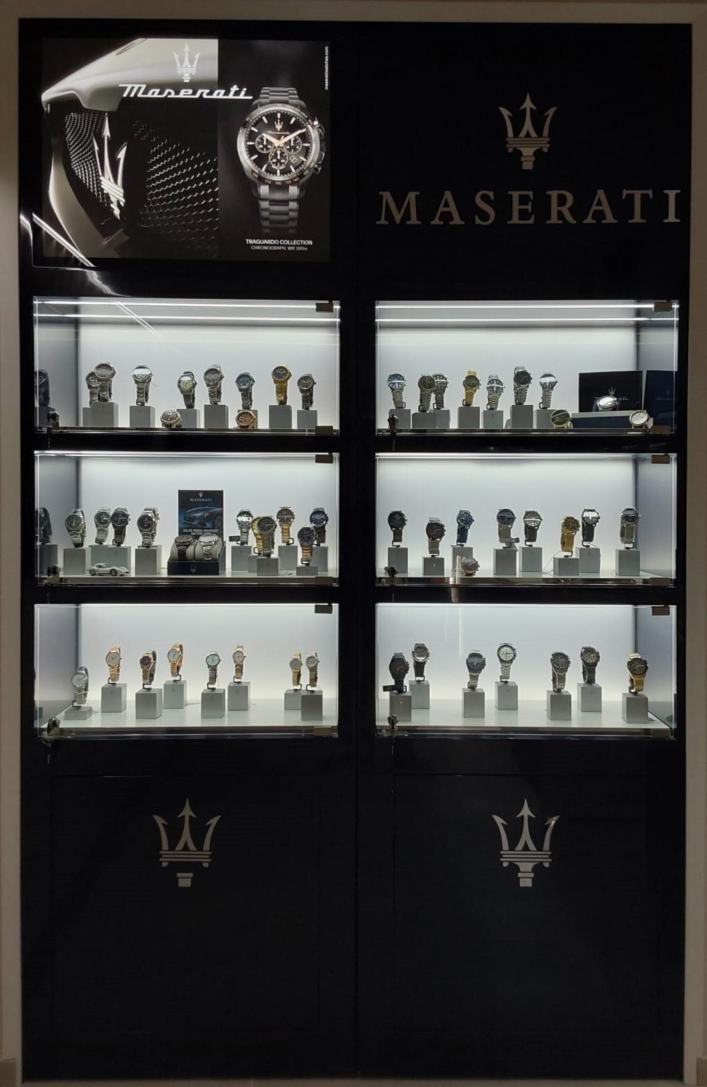 Vetrina per orologi Maserati con molti orologi in un negozio. Mobiletto nero con ripiani illuminati.