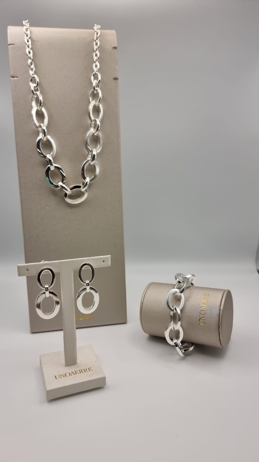 Set di gioielli in argento: collana, orecchini e bracciale su espositori di colore neutro.