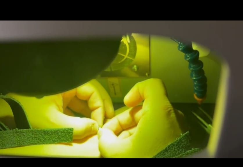 Mani che lavorano all'interno di una macchina laser, immerse nella luce gialla.