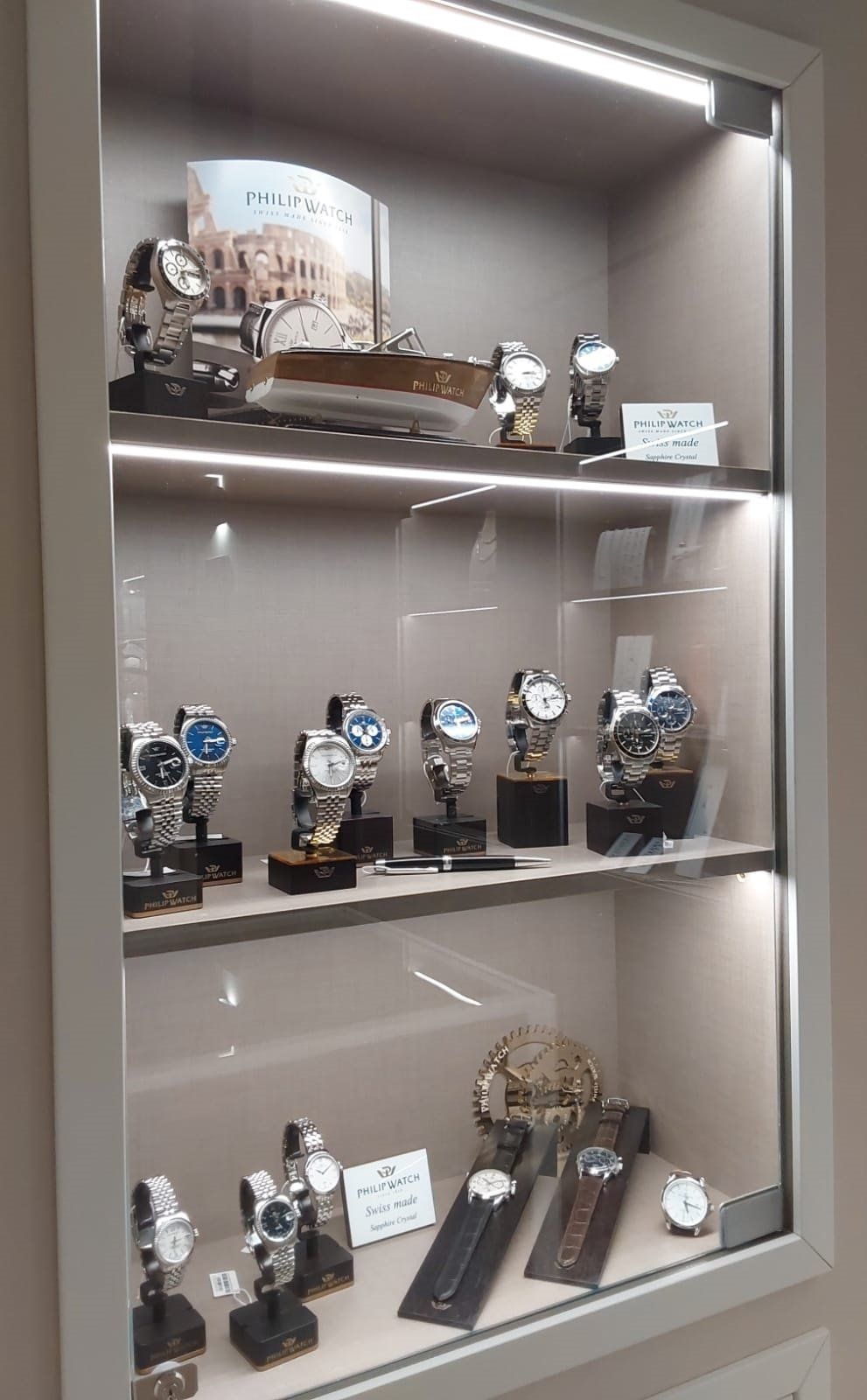 Vetrina in vetro con vari orologi esposti; interno illuminato da luci soffuse.