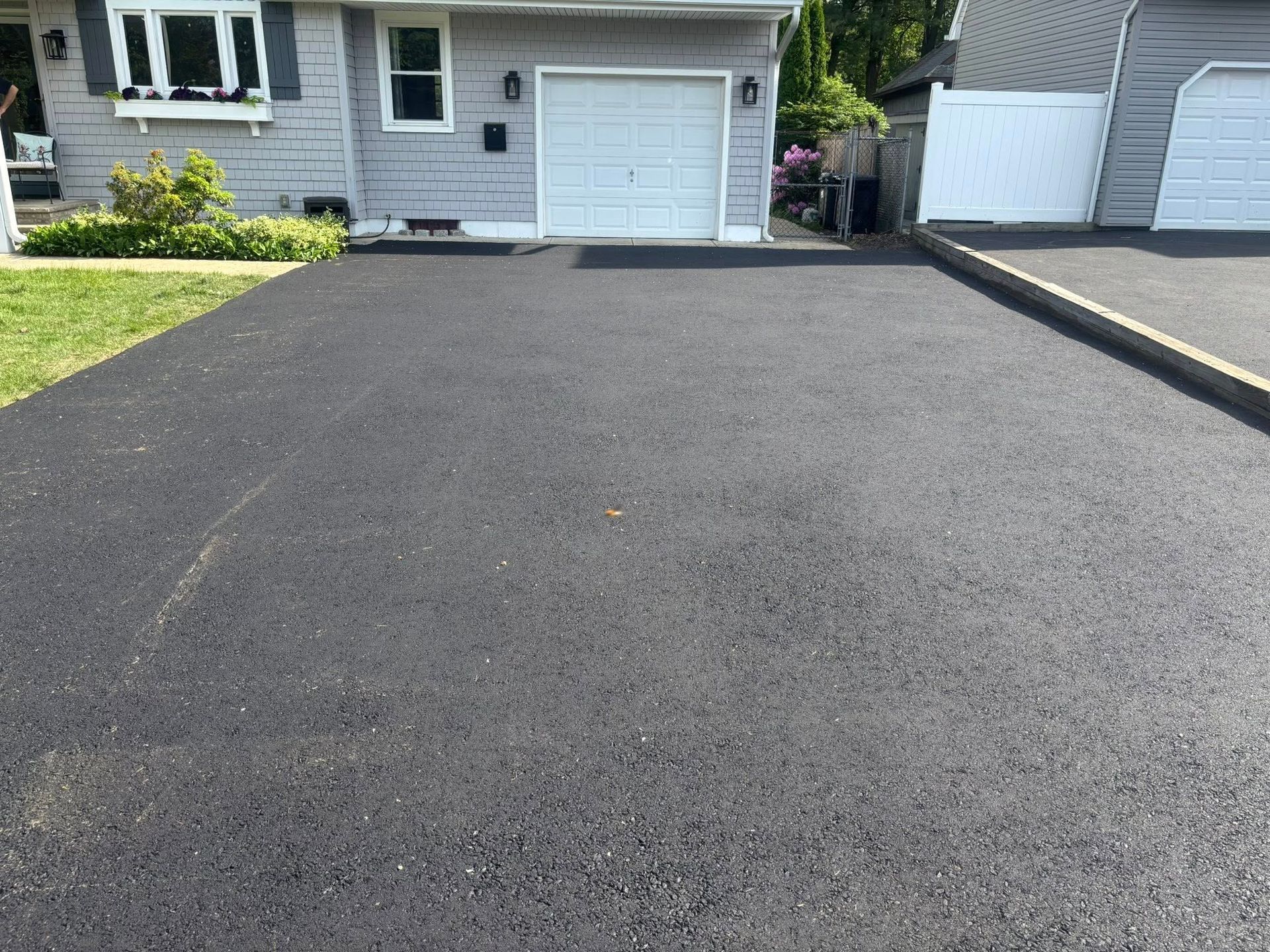 Black asphalt driveway in front of a gray house with a white garage door.