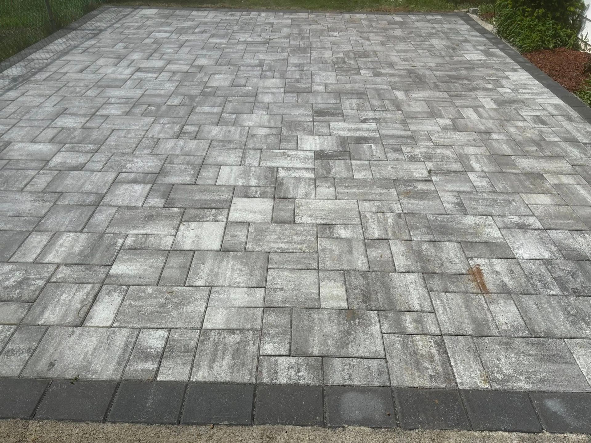 Gray and white pavers forming a driveway or patio with a dark border.