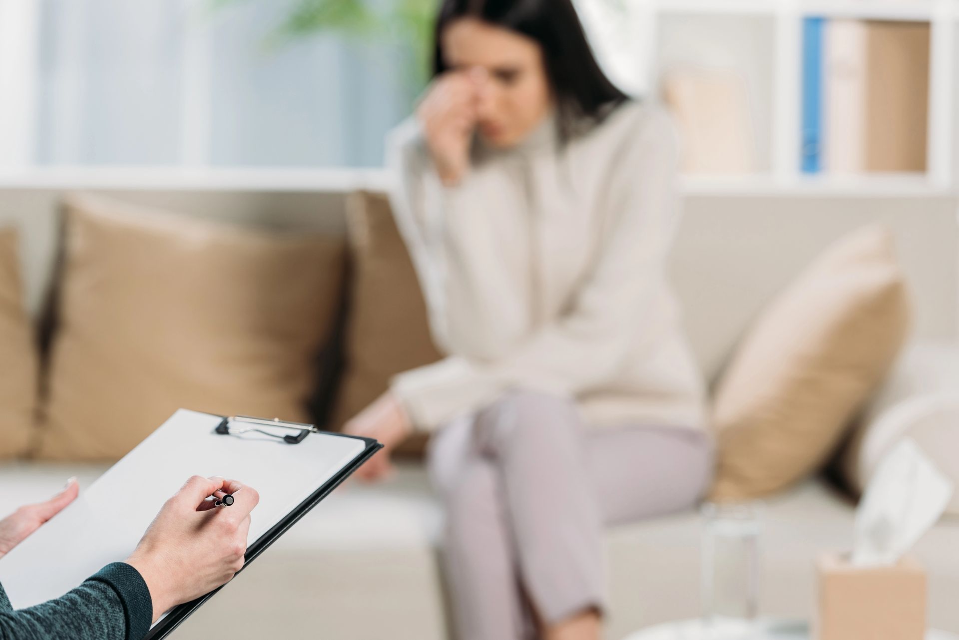 Un terapeuta prende appunti mentre un paziente, la cui immagine è sfocata, è seduto su un divano in una stanza.