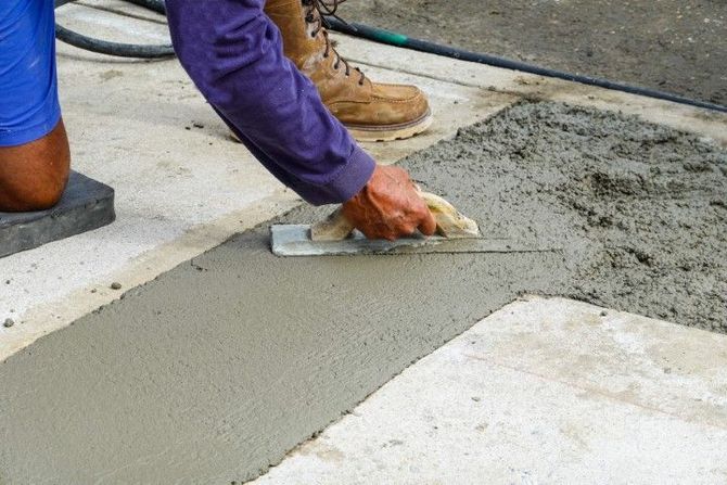 Worker smoothing wet concrete with a trowel near a sidewalk edge