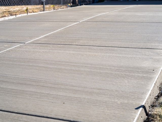 Empty concrete tennis court with painted boundary lines and a chain-link fence in the background