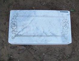 White engraved rectangular plaque with floral corners lying on dirt ground