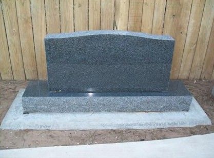Granite gravestone on a concrete base in front of a wooden fence