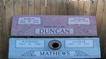 Two cemetery headstones, pink Duncan above blue Mathews, with engraved names and dates.