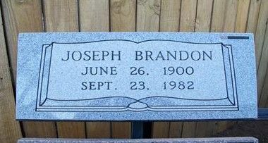 Joseph Brandon gravestone with name and dates, set against a wooden fence.