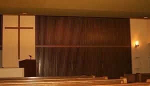 Church altar and pulpit with a large cross, wooden panel backdrop, and warm lighting