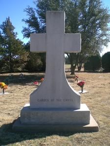 White cross gravestone in a cemetery with flowers and trees in the background