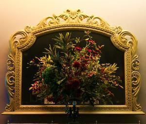 Ornate gold-framed floral arrangement with red and green flowers on a dark background