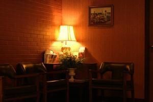 Dimly lit lounge with two chairs, a lamp, and a small table against wood-paneled walls