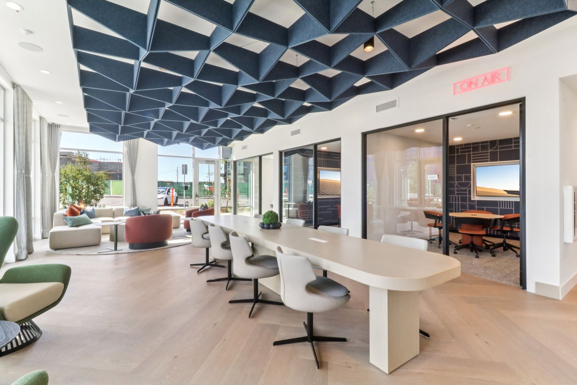 Modern co-working space with a long table, geometric ceiling, and glass-walled rooms.