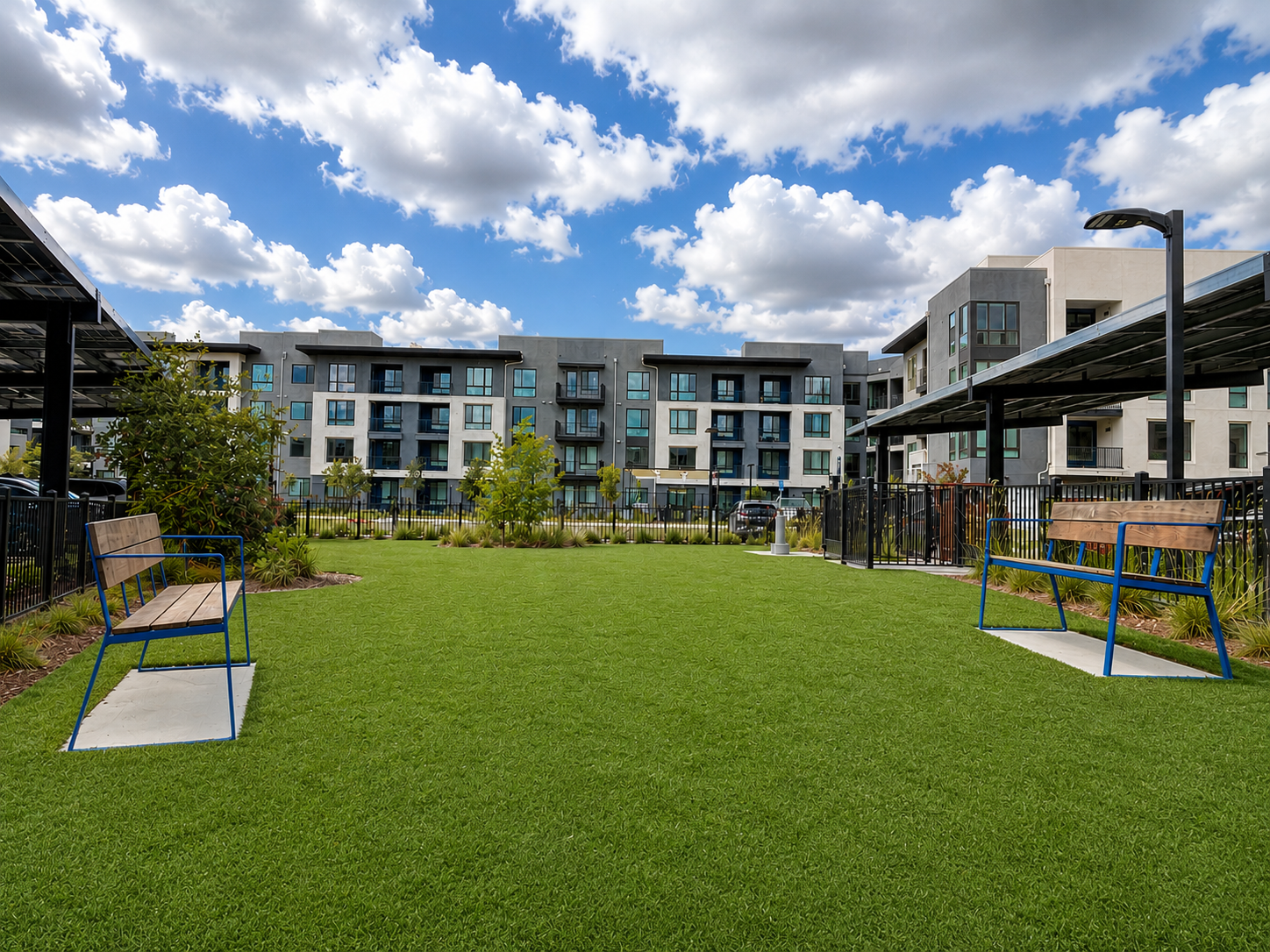 Apartment courtyard with green lawn, pergolas, and modern buildings under a cloudy sky
