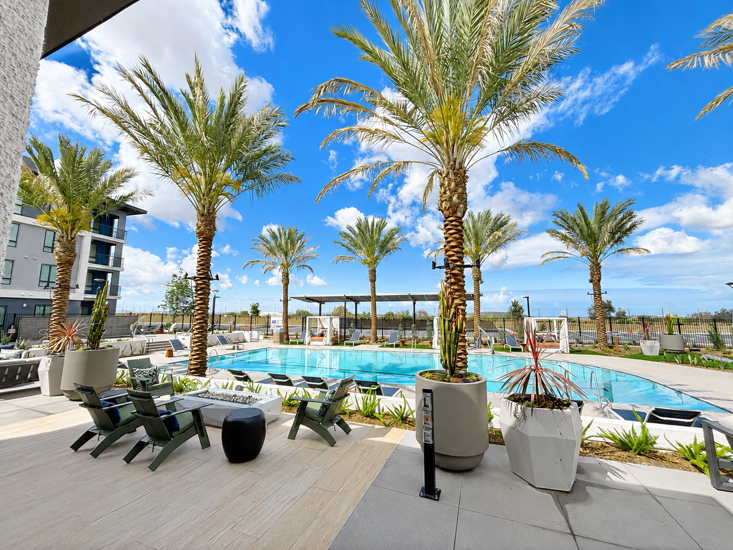 Palm-lined resort pool with lounge chairs, blue umbrellas, and a bright blue sky