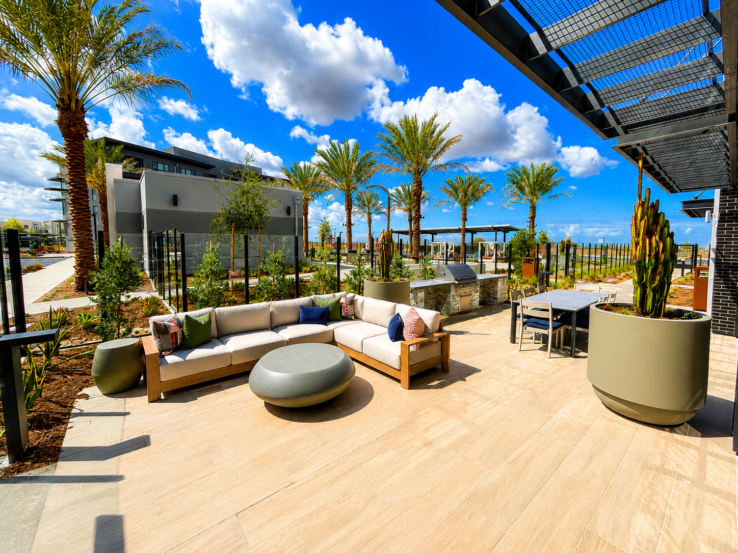 Modern outdoor patio with beige sectional seating, palm trees, and blue sky at a resort or rooftop terrace