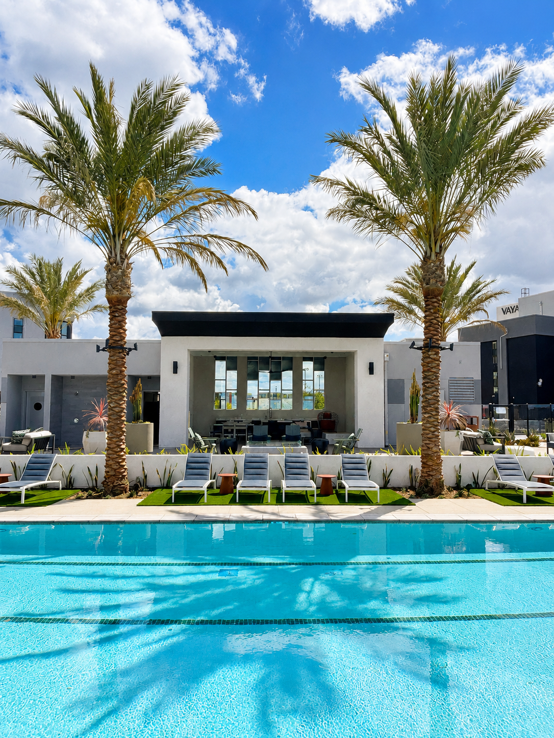 Modern resort pool with palm trees, lounge chairs, and a sleek white villa under a blue sky