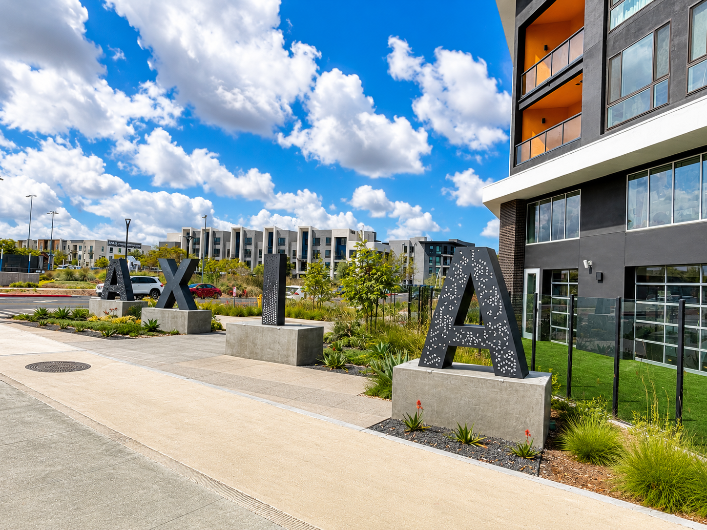 Modern apartment complex entrance with large black letters, concrete planters, and a bright blue sky