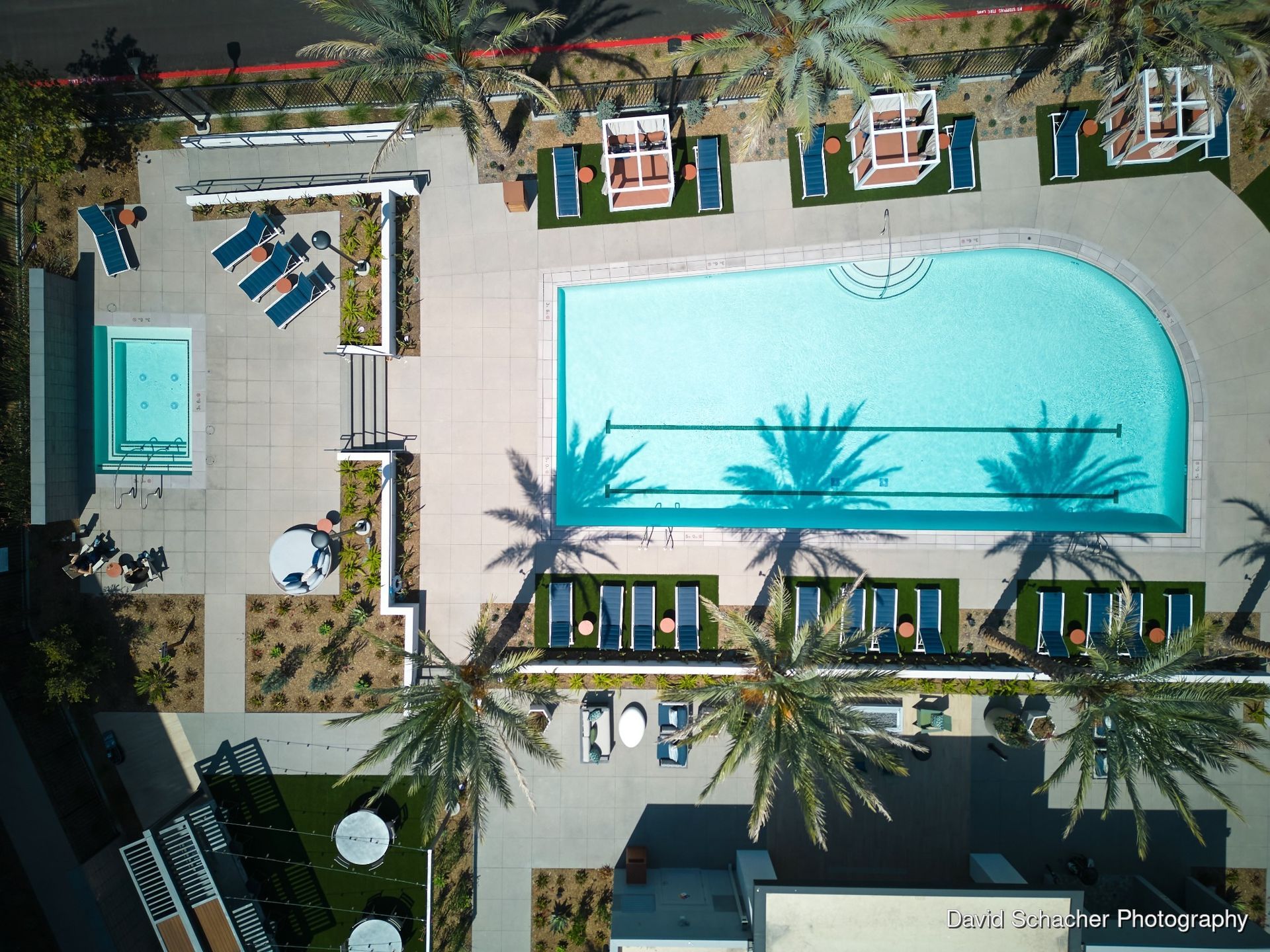 Aerial view of a resort pool with lounge chairs, palm trees, and a small cabana area.