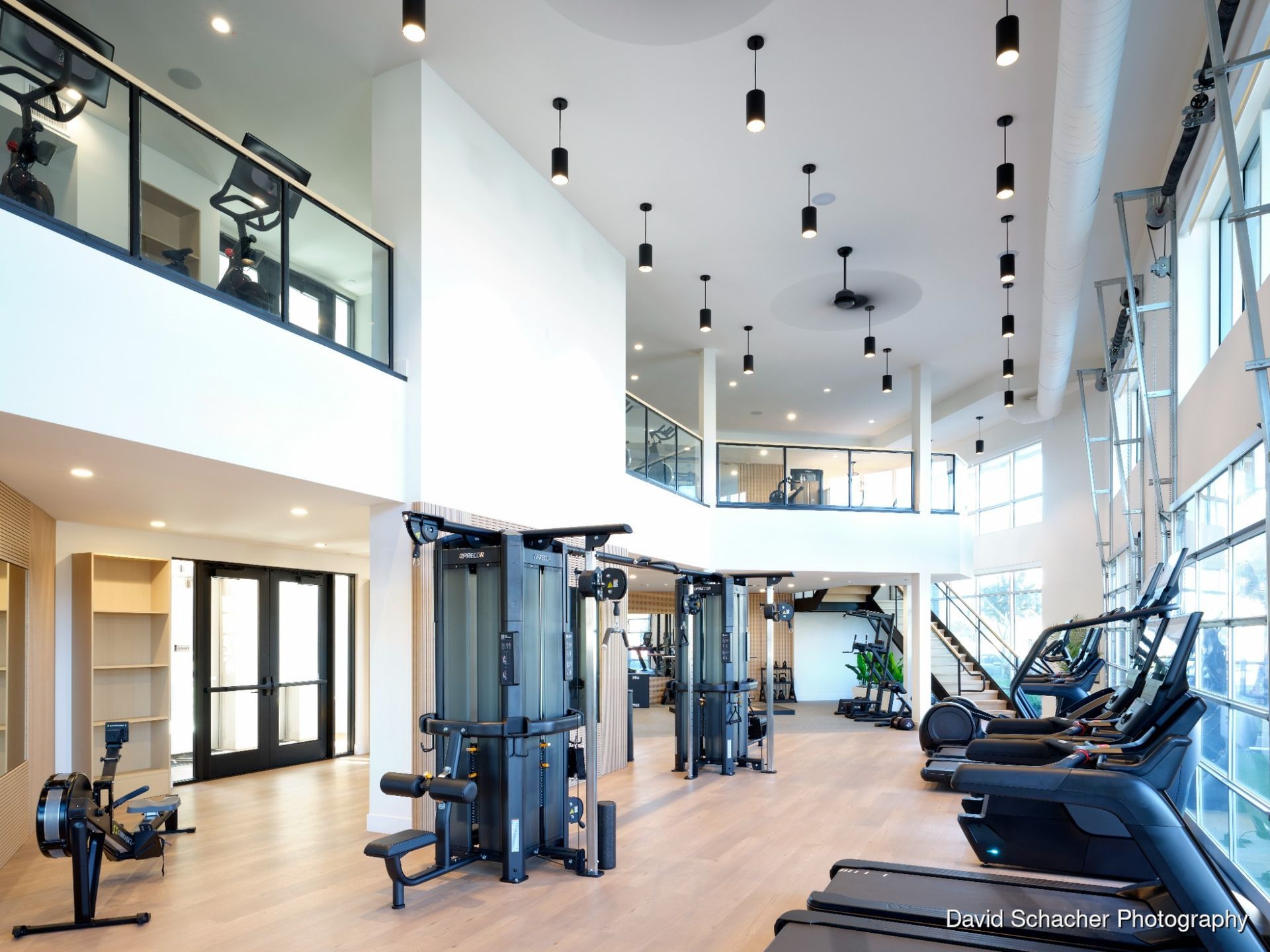 Gym interior with cardio machines, weight bench, and large windows.
