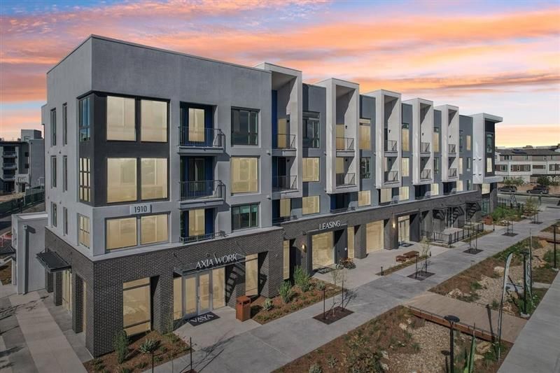Modern multi-story building with storefronts and outdoor walkway on a sunny day.