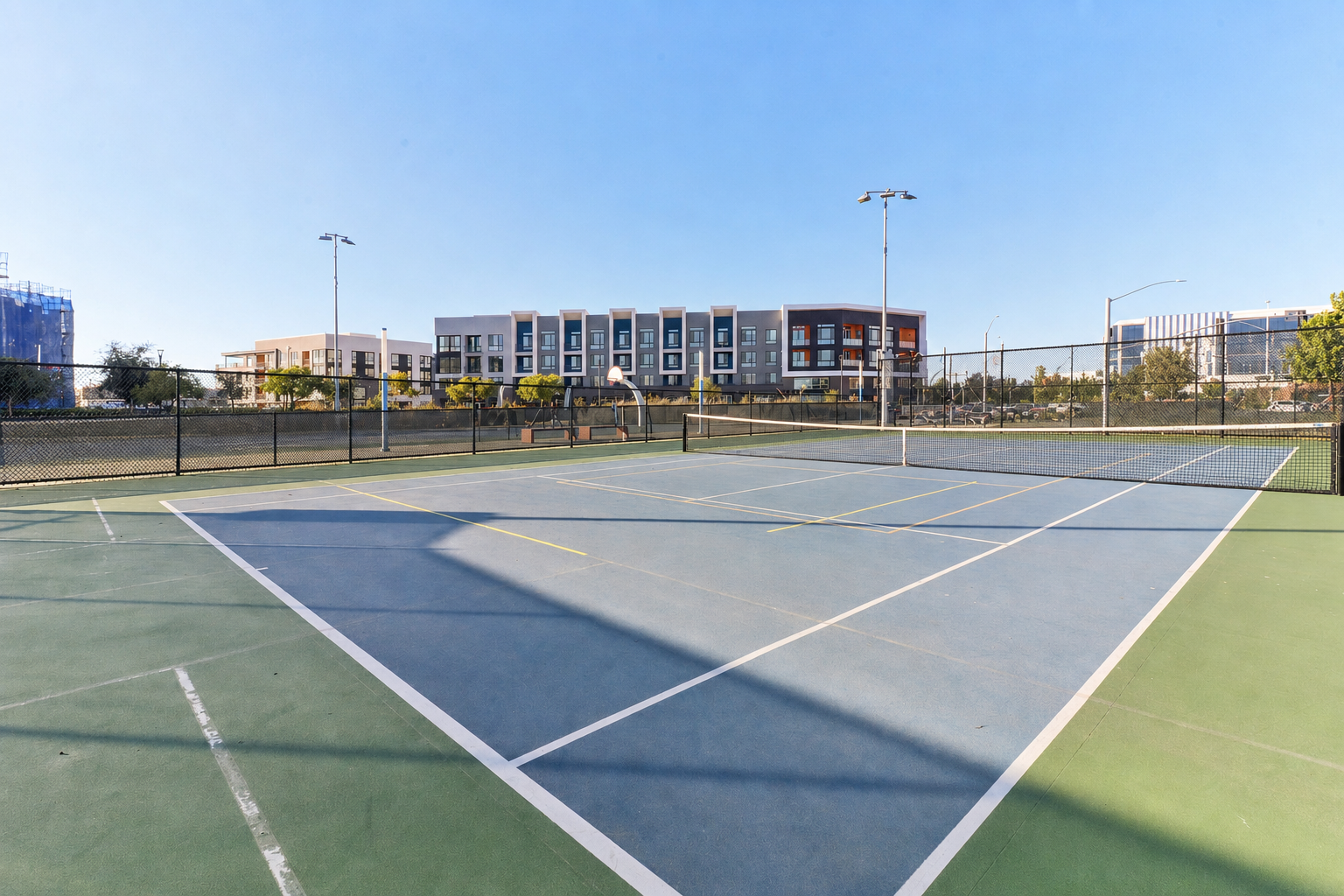 Tennis court with blue and green surface; modern apartment building in the background.