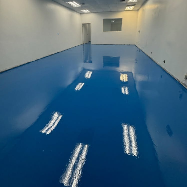 Empty room with glossy blue epoxy floor and white walls, reflecting ceiling lights