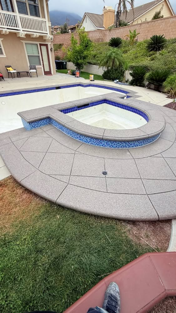 Backyard pool with a raised circular spa and blue-tiled coping beside a house and garden.