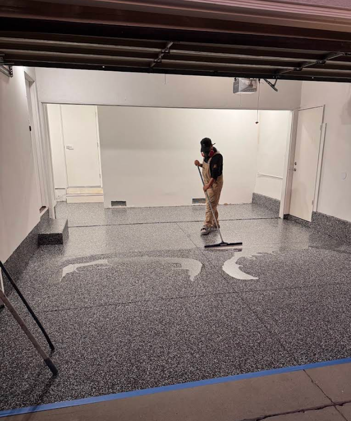 Person applying epoxy coating to a garage floor with a speckled gray finish