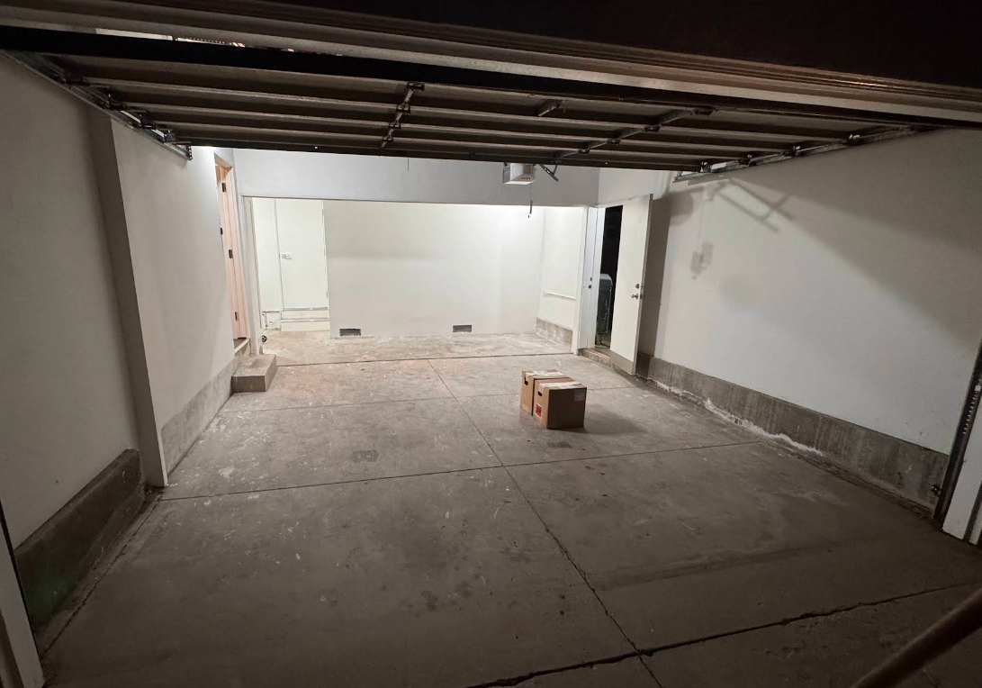 Empty unfinished basement or garage with concrete floor, exposed ceiling beams, and a small cardboard box.