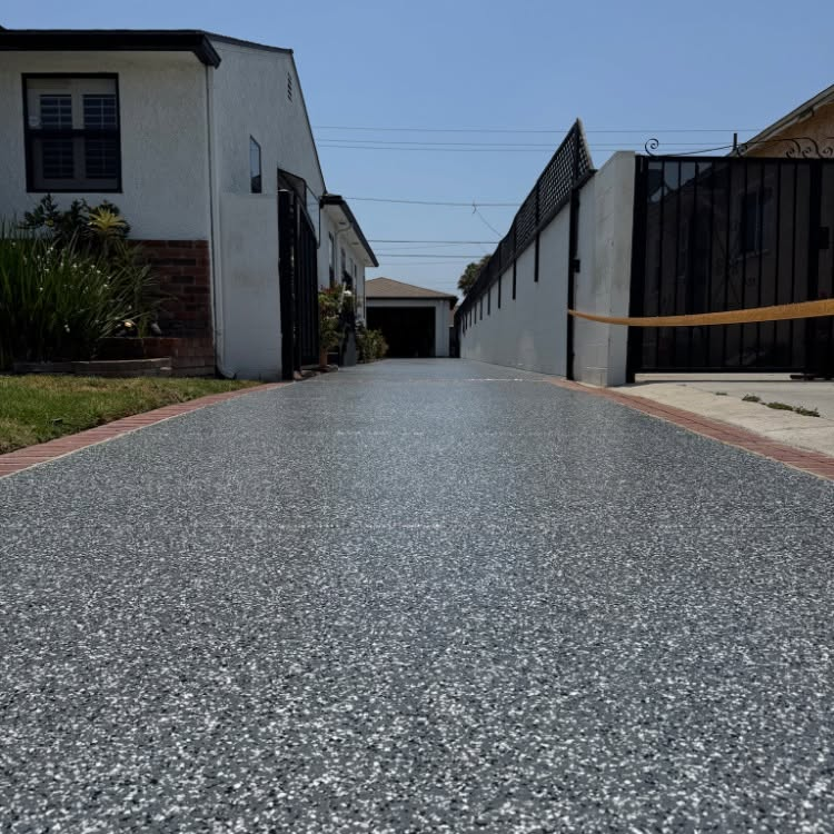 Low-angle view down a paved residential driveway between white buildings and black fences under a clear sky