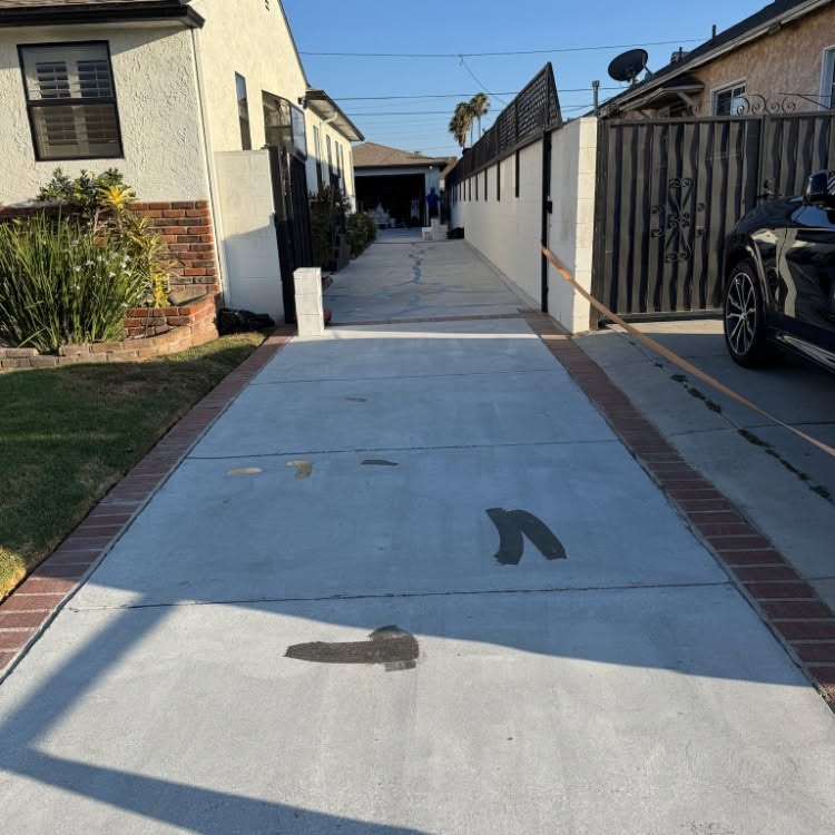 Apartment walkway with fresh concrete, brick borders, and parked car beside a gated fence