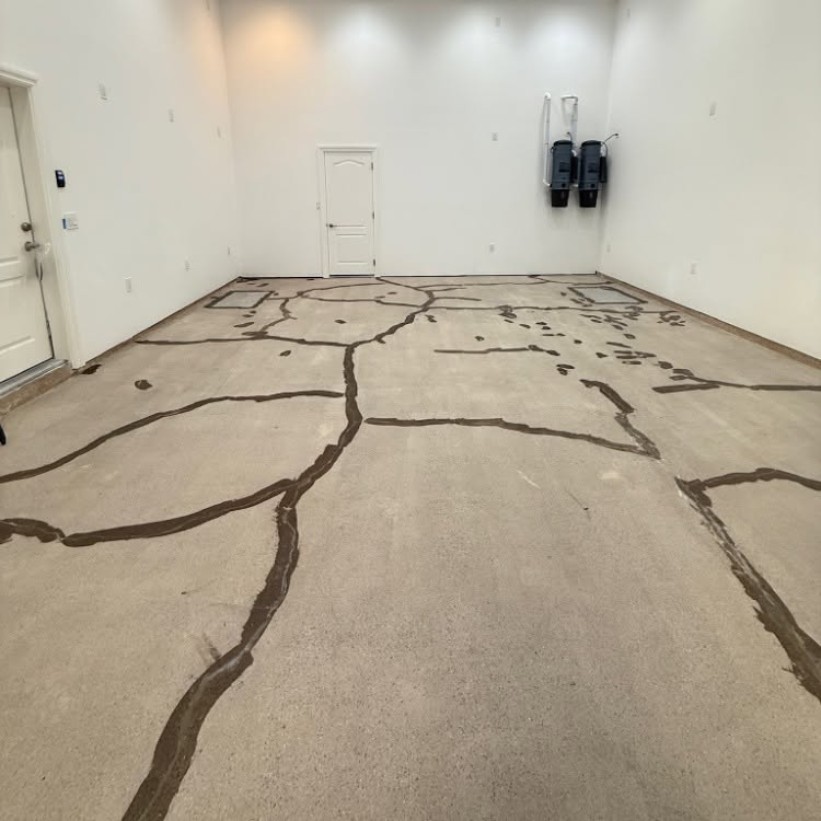 Empty white room with beige floor covered in dark crack-like lines and wall-mounted devices on the right.