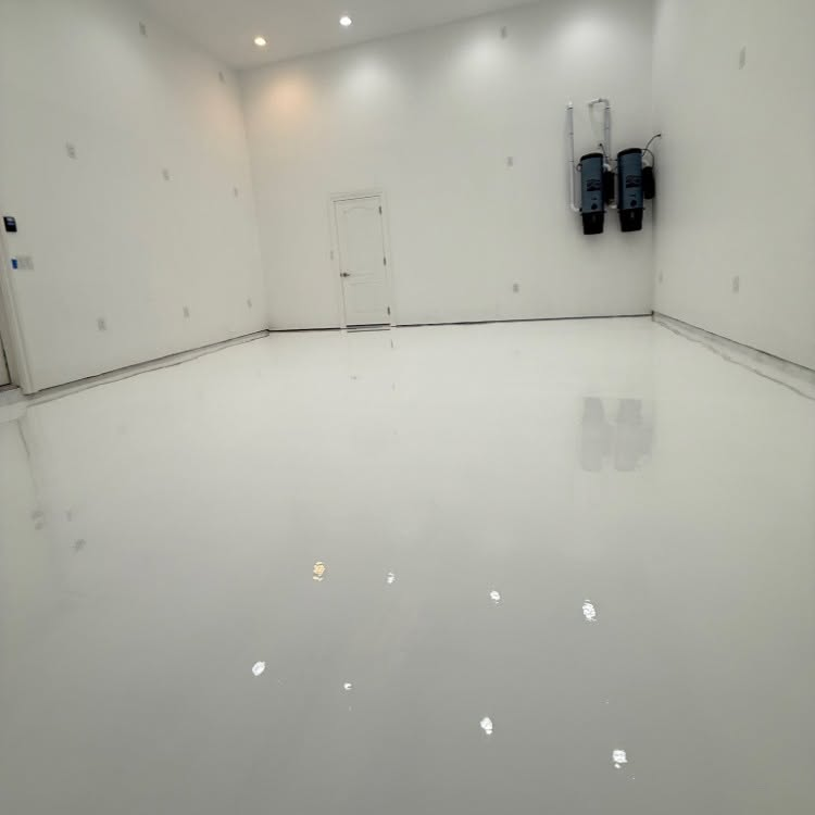 Empty white room with glossy floor, recessed lights, and two wall-mounted devices on the right.