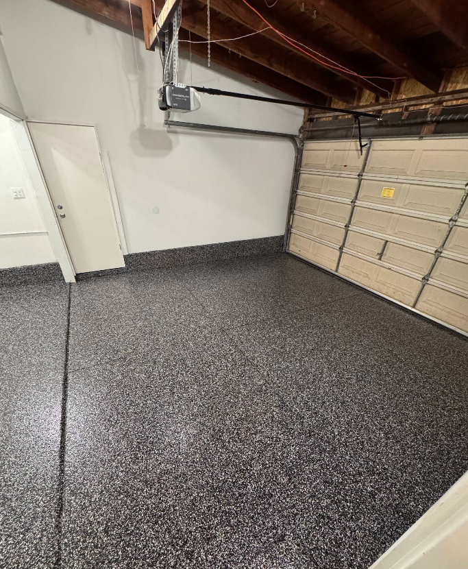 Empty garage interior with speckled epoxy floor, white walls, and a closed garage door.