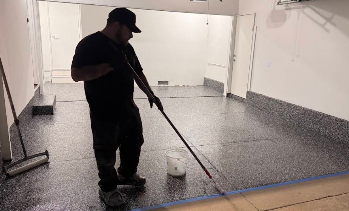 Person sweeping a wet floor in a large empty room with white walls