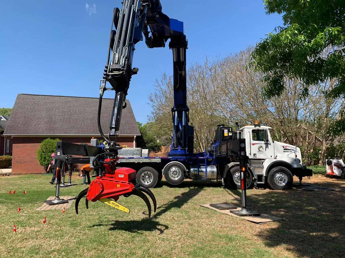 A large truck with a crane attachment in a yard. Red and blue crane poised to grab something. Sunny day.