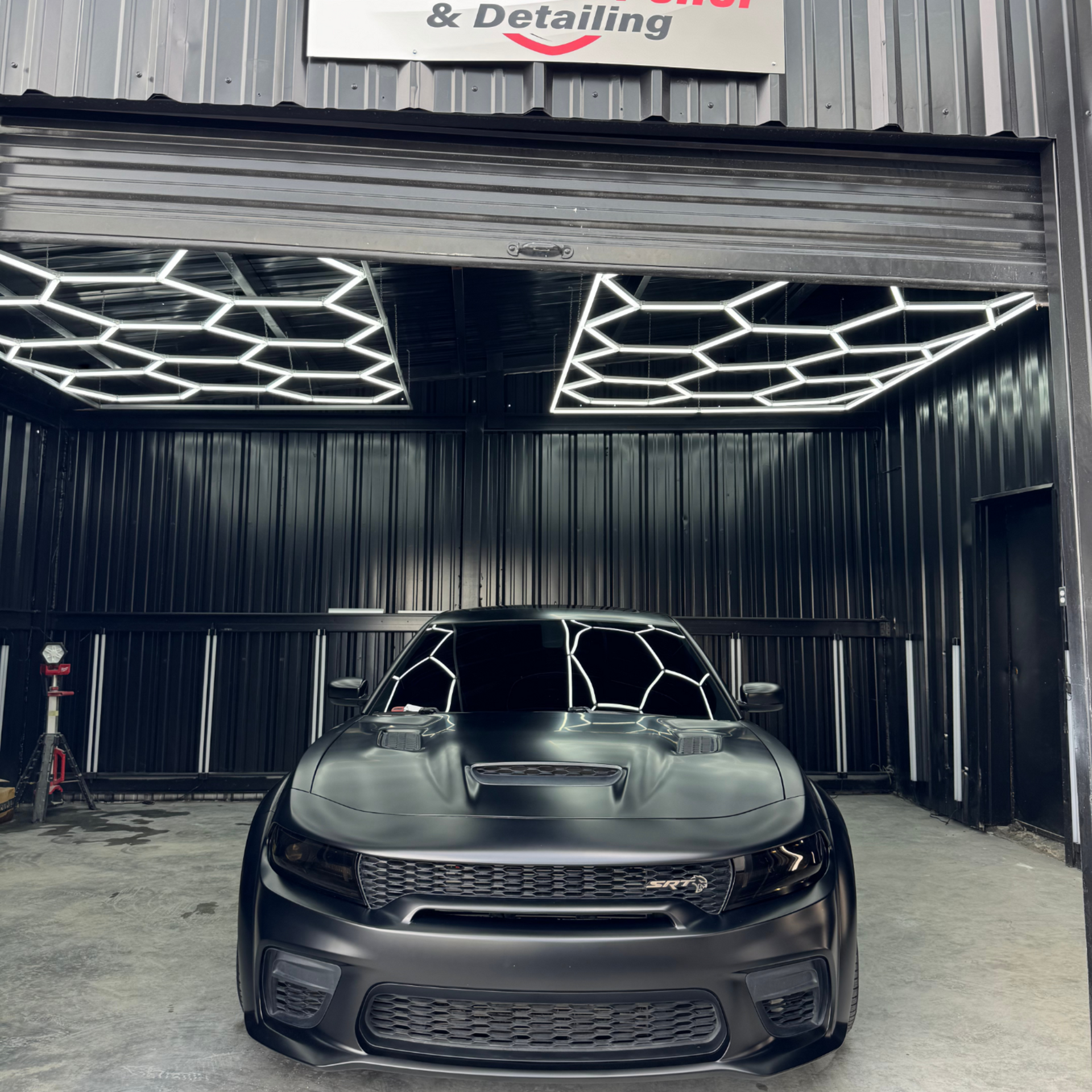 Black Dodge Charger in a detailing bay, illuminated by hexagonal lights.
