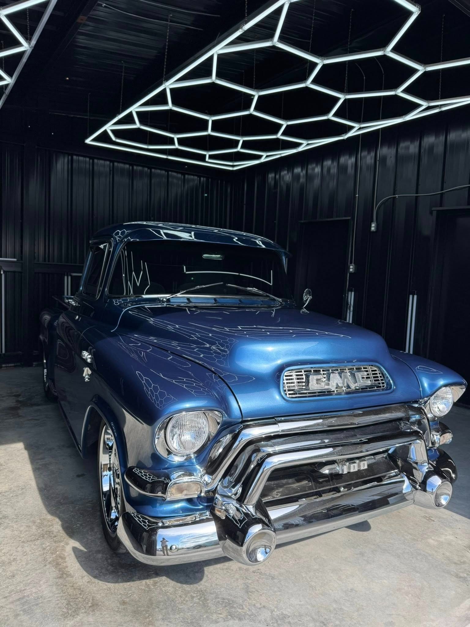 Blue vintage GMC truck with chrome accents, parked in a modern garage with hexagonal lights.