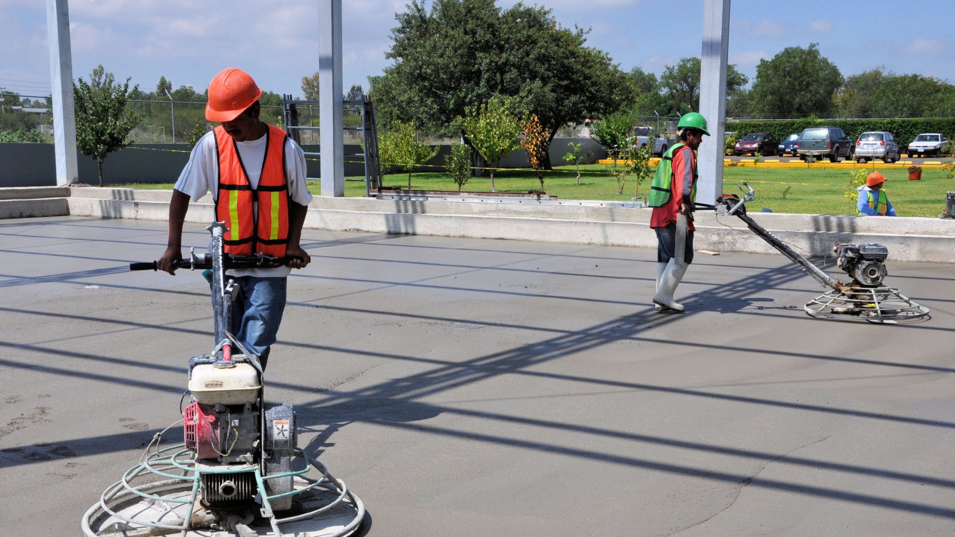 Two construction workers are working on a concrete floor