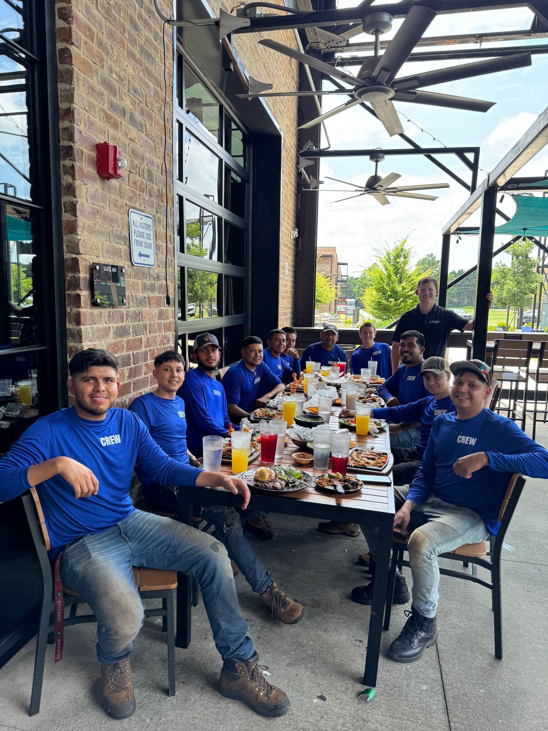 Group of men in blue shirts and jeans at outdoor restaurant table.