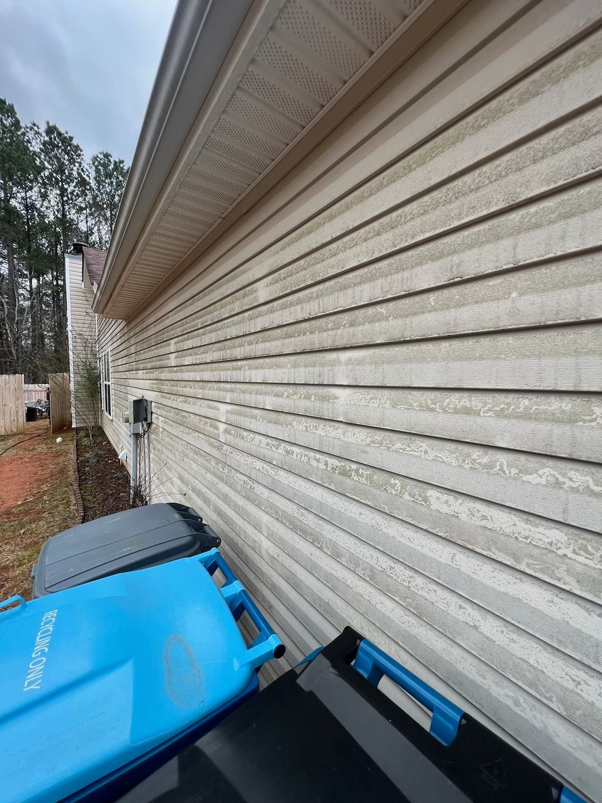 A blue trash can is sitting on the side of a house.