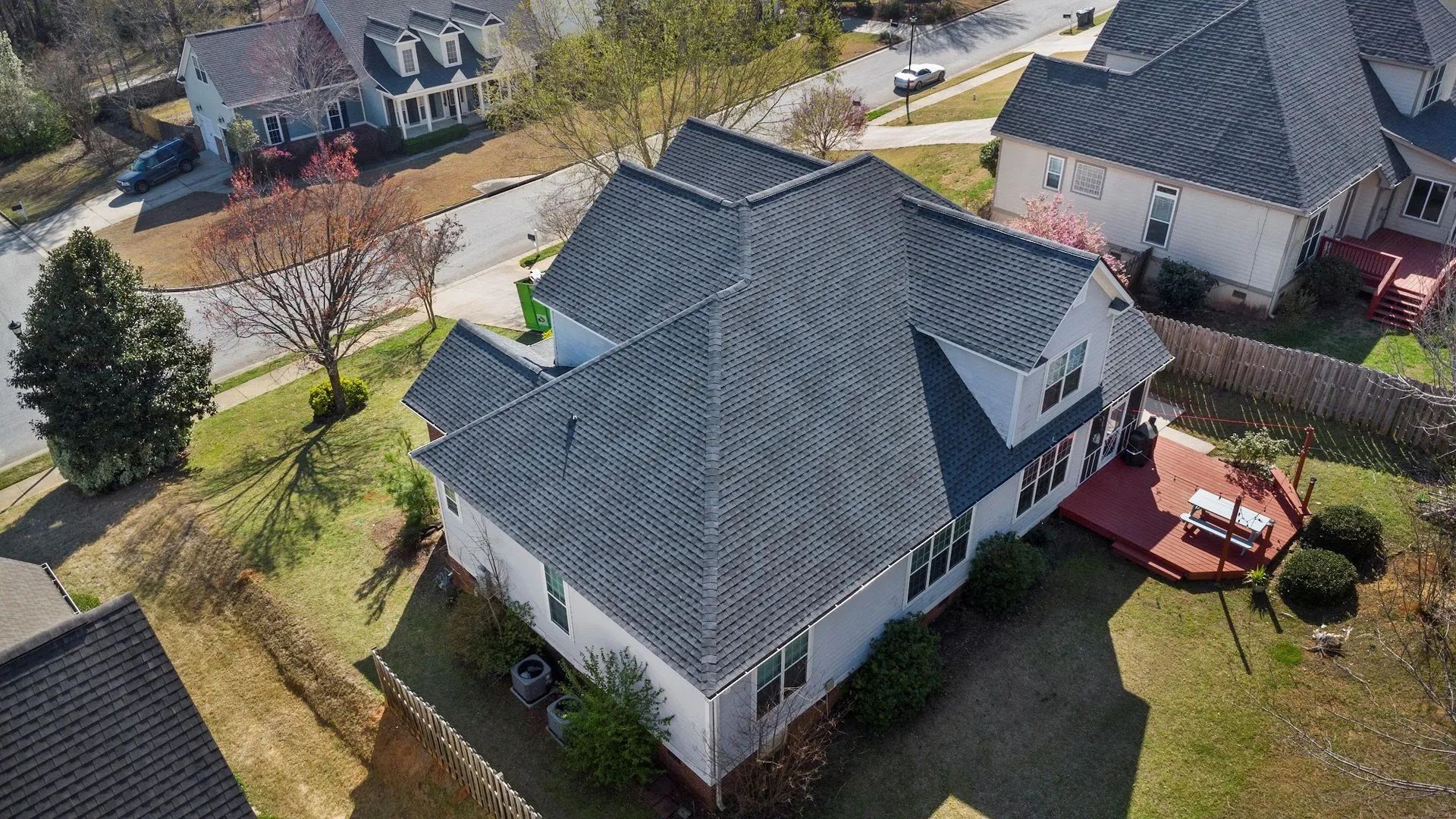 Aerial view of a gray-roofed house with a red deck in a suburban neighborhood.