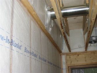 Isolation murale étiquetée « Blow-In-Blanket » entre les poutres en bois. Une bâche en plastique recouvre l'isolant.
