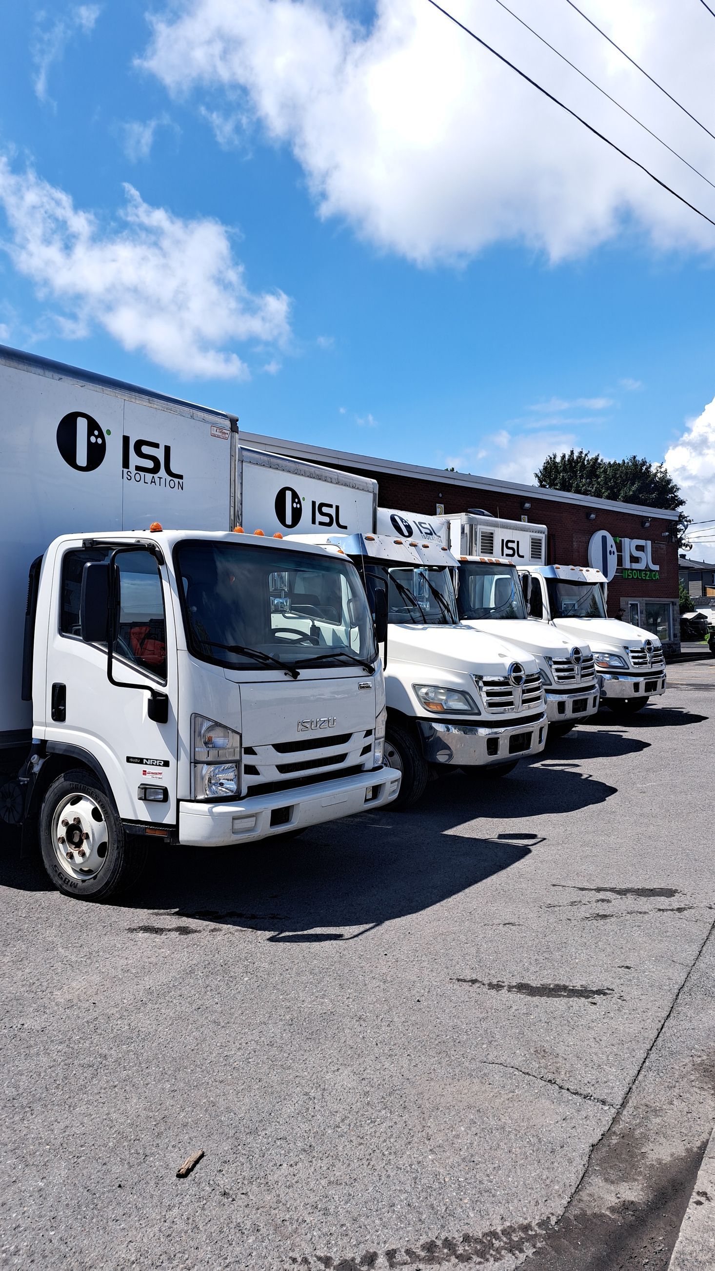 Des camions ISL blancs garés en rang sur un parking gris goudronné sous un ciel bleu nuageux.