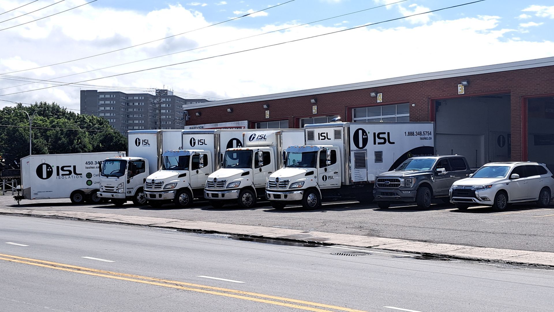 Une rangée de camions de déménagement blancs et deux voitures garées devant un bâtiment portant le logo « ISL ».