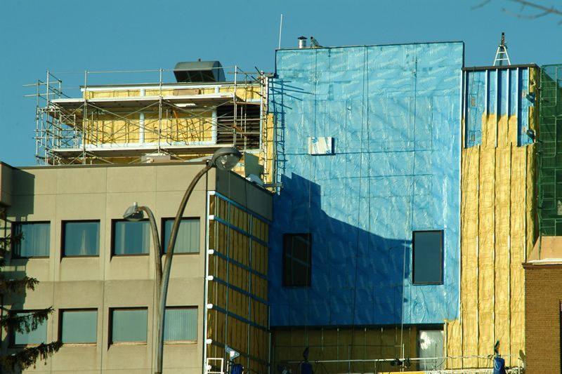 Façade d'un bâtiment en construction, avec isolation apparente dans des tons de jaune et de bleu.
