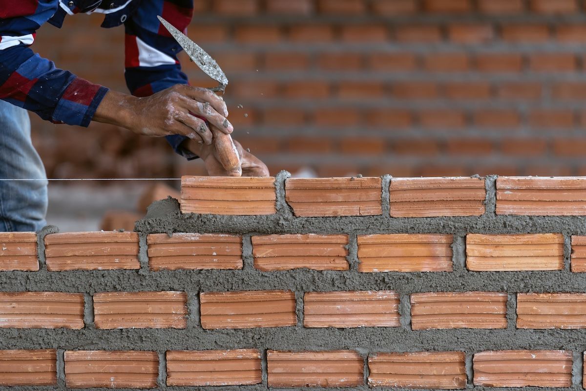 Hands laying red bricks on a brick wall with mortar, close-up construction scene