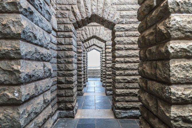 Stone corridor with repeated arches and a bright opening at the far end